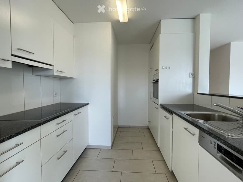 Modern kitchen with white cabinets, stainless steel sink, and built-in oven. Granite countertops and tiled flooring.