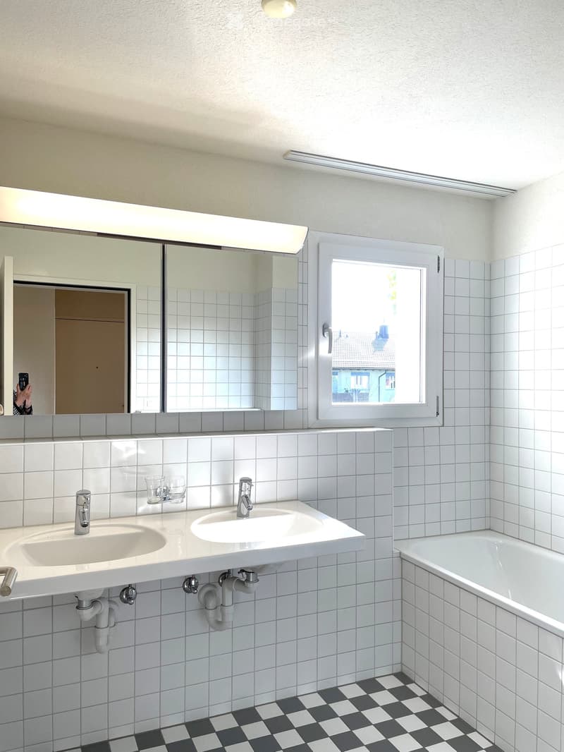 modern bathroom, white tiles, black and white checkered floor, large mirror, double sinks, bathtub, window