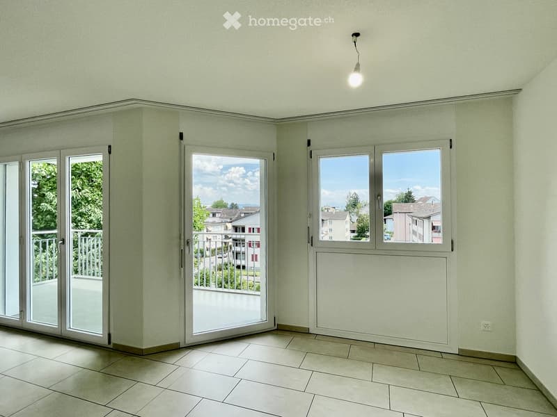 Empty room with tiled floor, large windows, and sliding glass doors leading to a balcony.