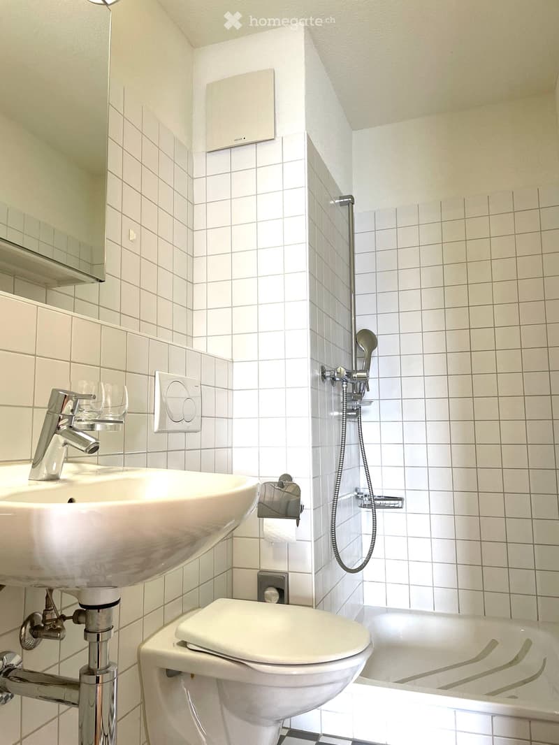 White tiled bathroom with shower, sink, and toilet