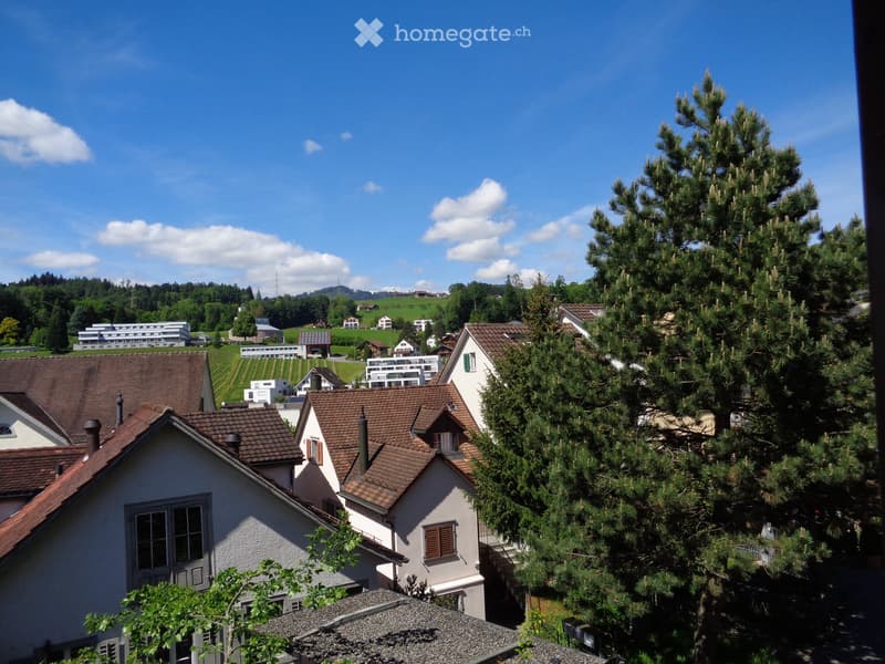 A scenic view of a residential area with multiple houses, surrounded by trees and greenery under a clear blue sky.