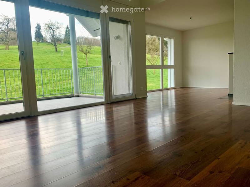Empty room with wooden flooring, large glass sliding doors leading to a balcony, and a view of a green lawn.