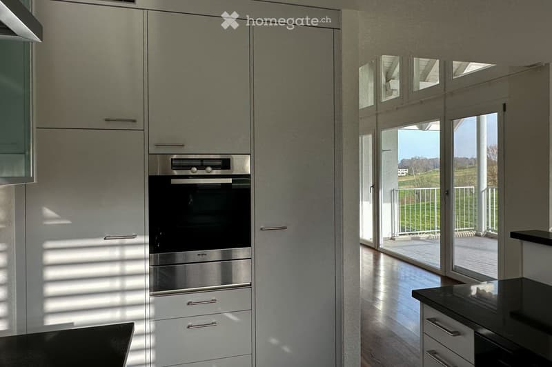 Modern kitchen with white cabinets, stainless steel oven, and large windows offering a scenic view.