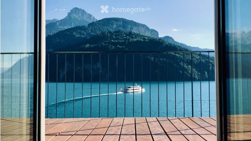Balcony with wooden decking, metal railing, and scenic mountain and lake view.
