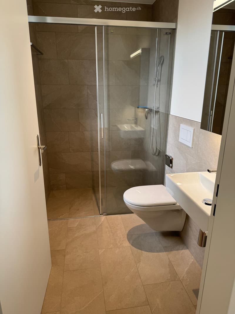 Modern bathroom with beige tiles, a toilet, a sink, and a glass-enclosed shower stall.