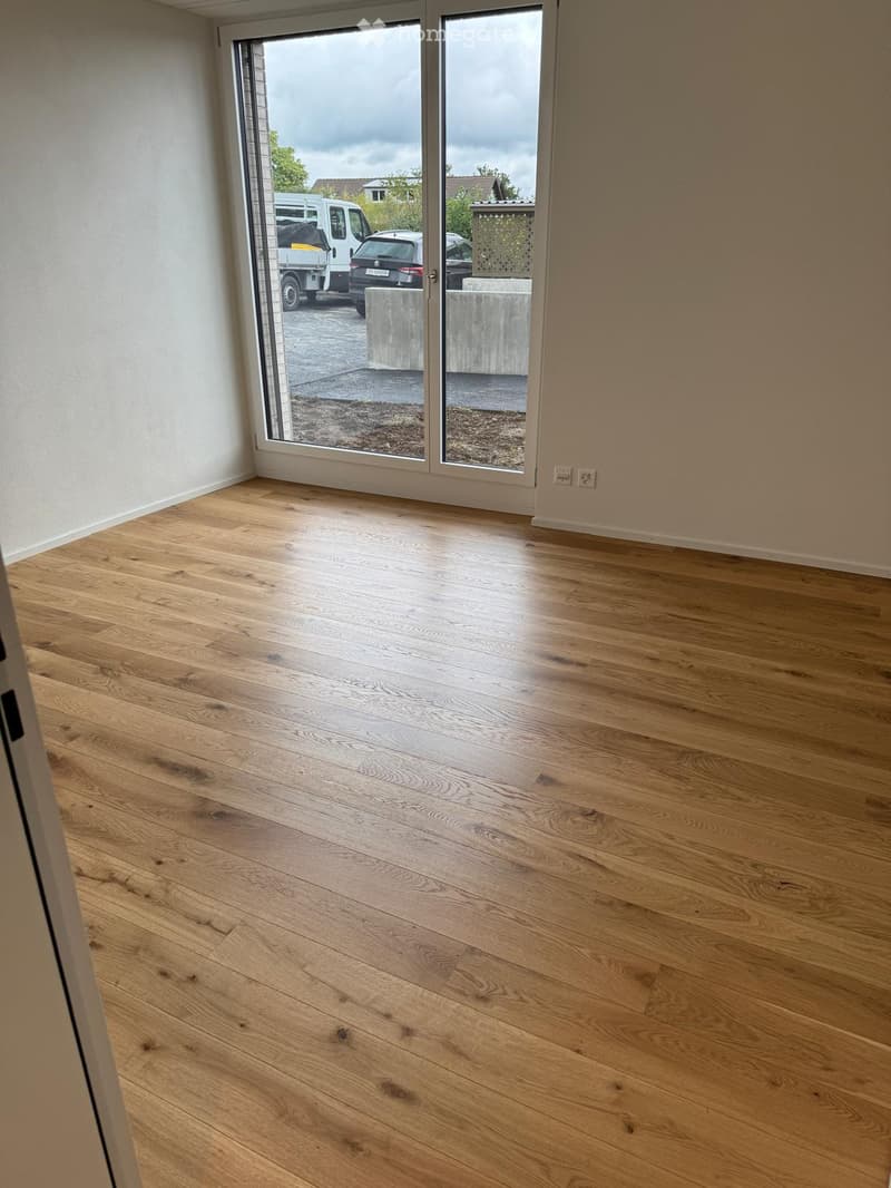 Empty room with light wooden flooring and large sliding glass doors leading to an outdoor area.