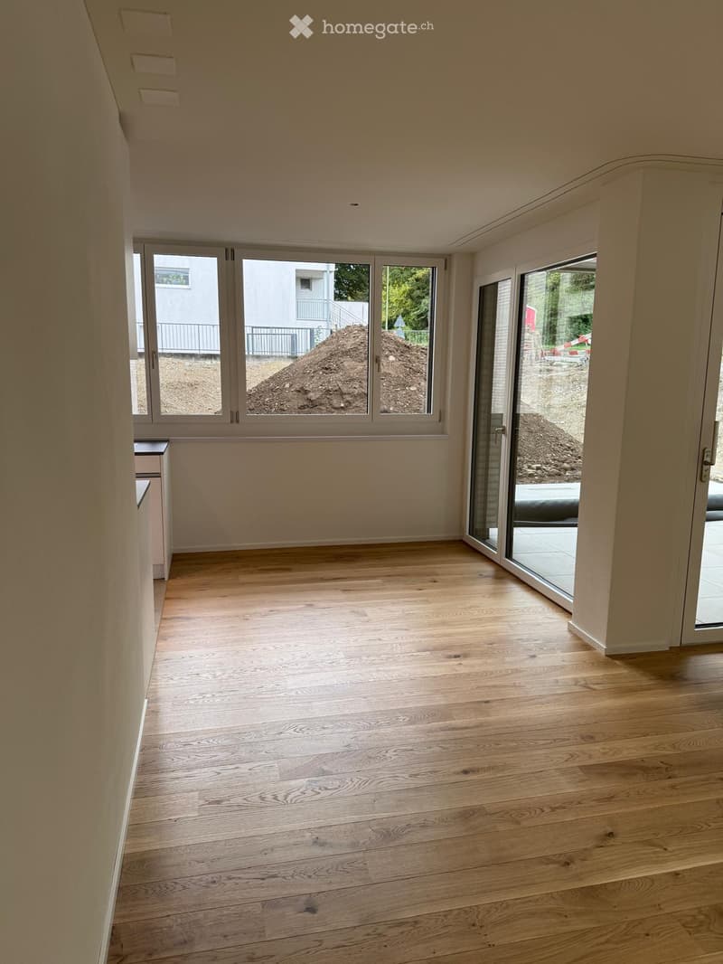 Empty room with light wooden flooring, large windows, and sliding glass doors leading to an outdoor area.