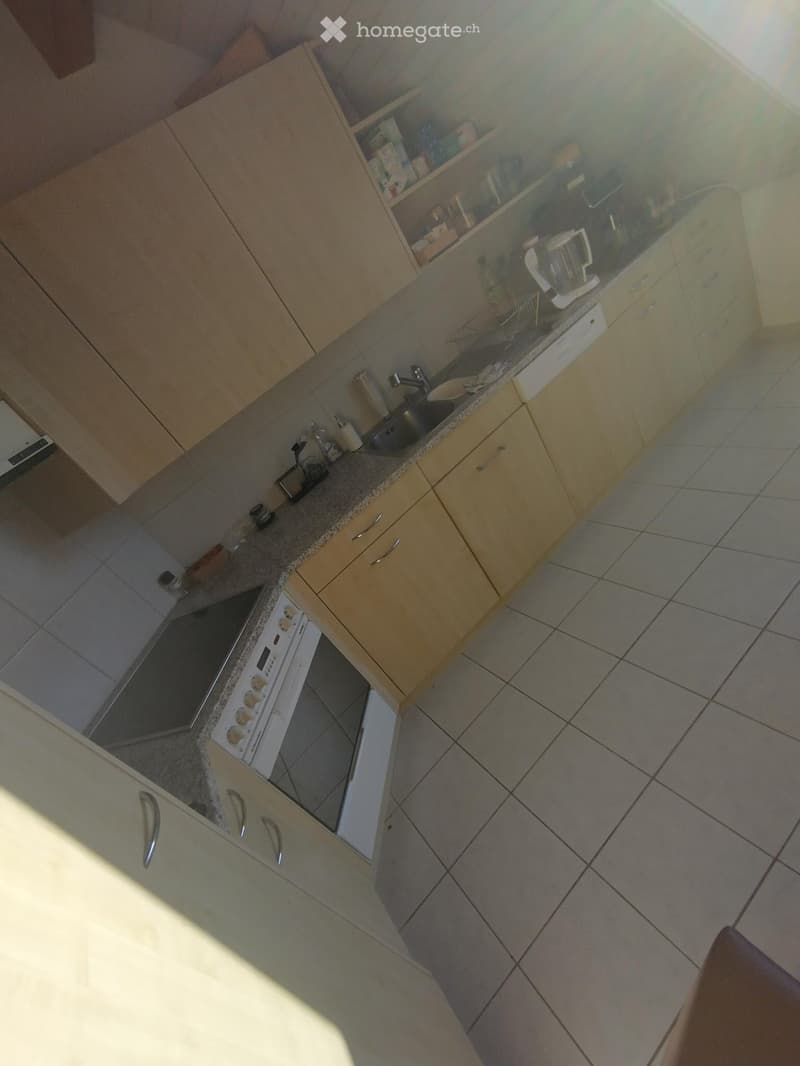A modern kitchen with light wooden cabinets, a stainless steel sink, a white oven, and a blender on the counter.
