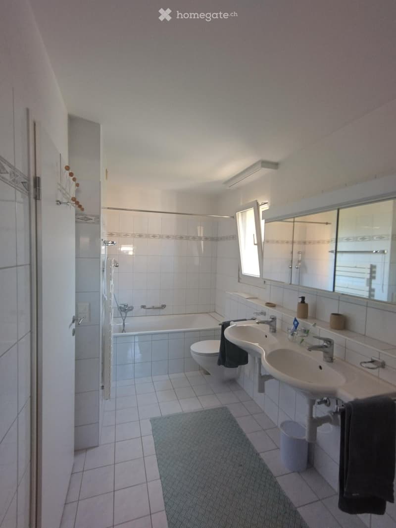 Modern bathroom with white tiles, double sink, bathtub, toilet, large mirror, and a shower area with a glass door.