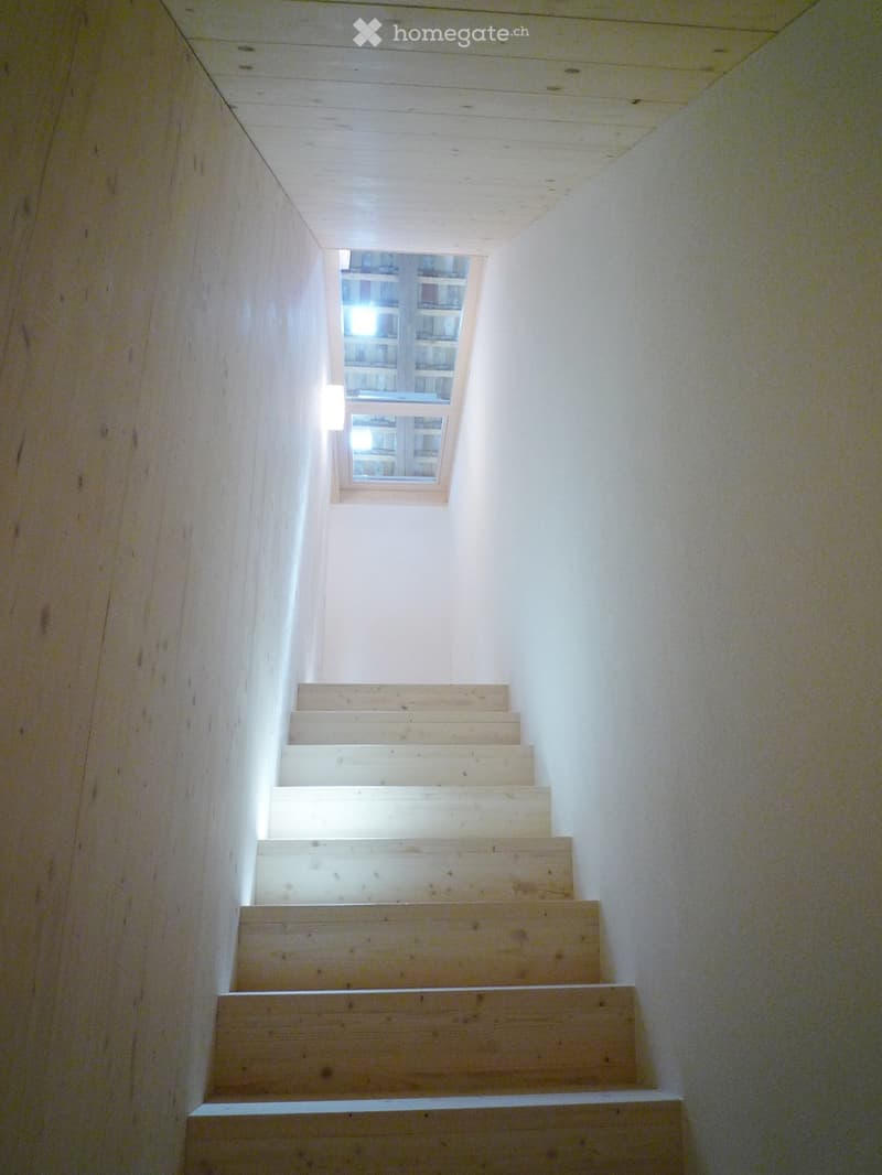 Wooden staircase with white walls and a small window at the top, allowing natural light into the hallway.