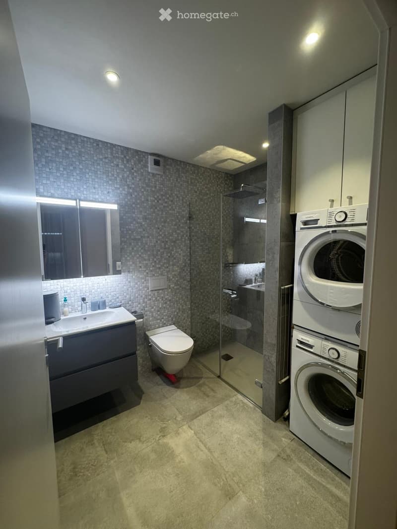 modern bathroom with tiled walls, glass shower enclosure, gray vanity, built-in sink, and stacked washing machines