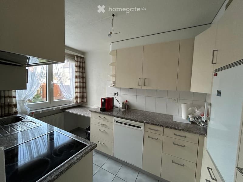 Modern kitchen with white cabinets, granite countertops, and stainless steel appliances including a stove, sink, and dishwasher. A coffee maker sits on the counter along with a paper towel roll and other small items.