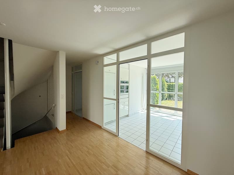 Empty room with wooden flooring, large glass sliding doors leading to a tiled patio, and a visible staircase in the background.