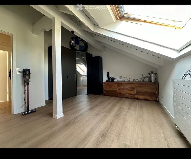 Bright attic room with wooden flooring, slanted ceilings, skylights, and a wooden dresser with decorative items on top.
