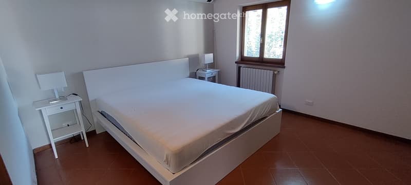 modern bedroom with white walls, brown tiles, large bed, two bedside tables, two lamps, heater, and a window