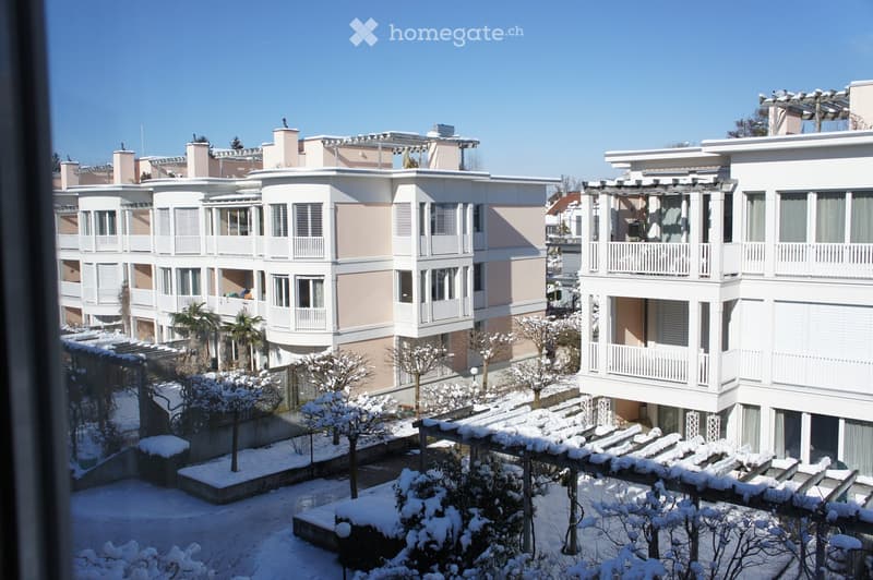 A multi-story residential building complex with balconies and snow-covered ground and trees.