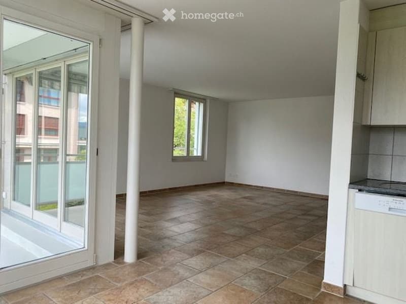Empty room with tiled floor, white walls, large window, and sliding glass door leading to a balcony.
