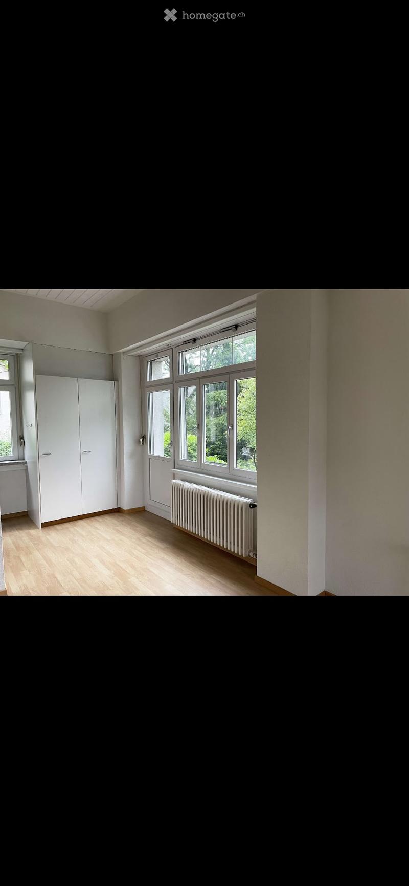 Empty room with wooden flooring, white walls, large windows, radiator, and white closet.