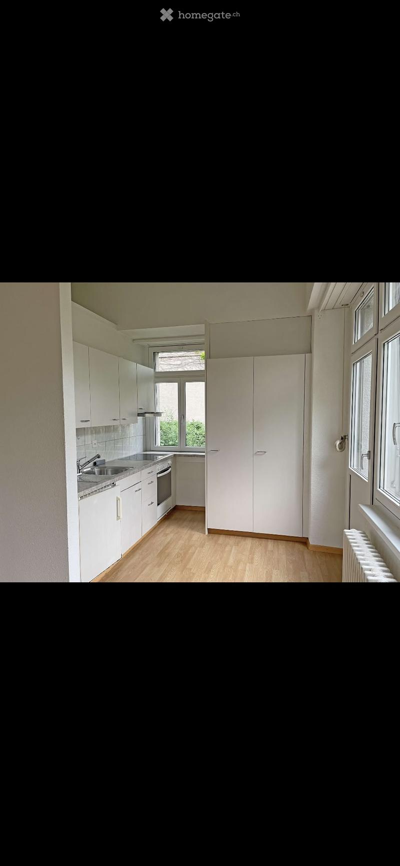 Modern kitchen with white cabinets, wooden flooring, and stainless steel appliances including a sink, faucet, and oven.