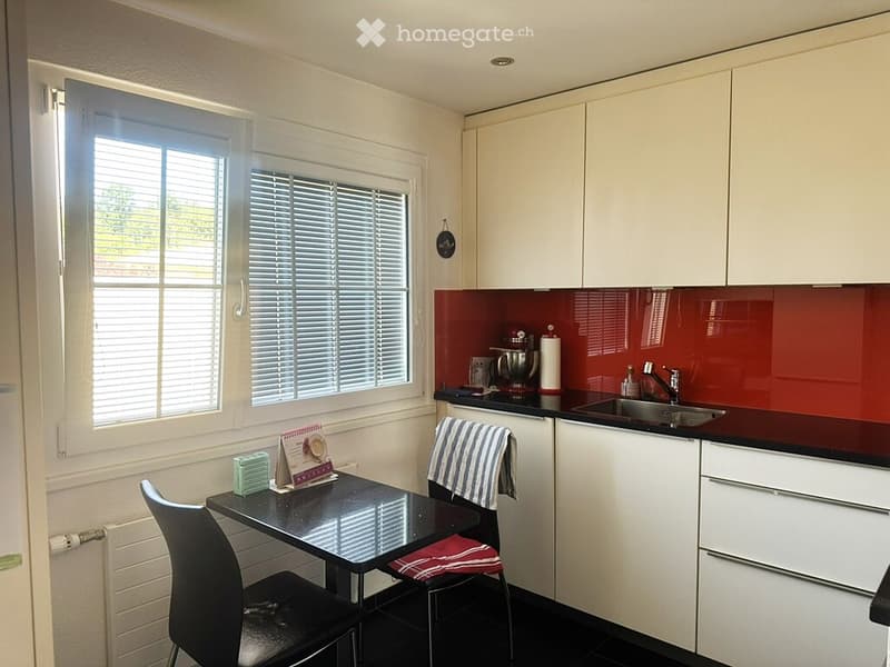 Modern kitchen with white cabinets, red backsplash, black countertops, and a small dining area with a black table and chairs.