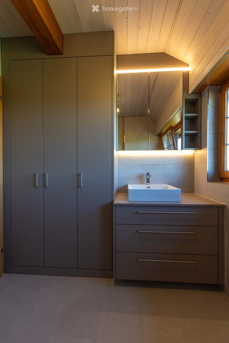 Modern bathroom with a white sink, large mirror with built-in lighting, and grey cabinets with sleek handles.