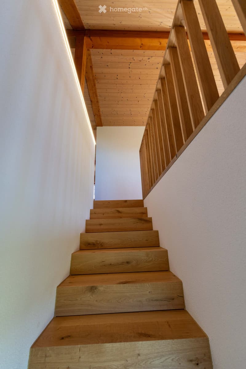 Wooden staircase with a modern design, featuring built-in lighting along the walls and a sleek wooden handrail.