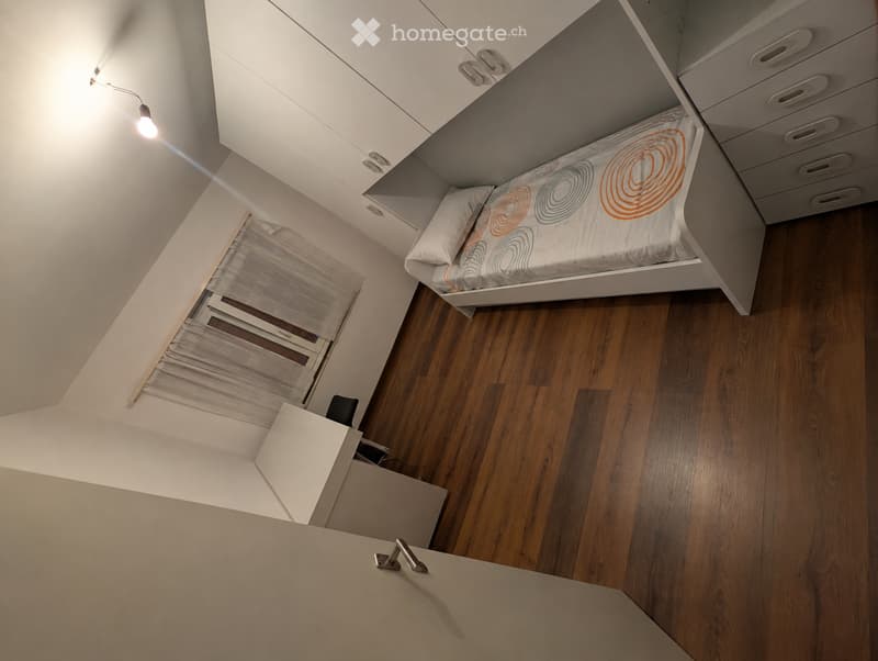 Modern, compact bedroom with a single bed, nightstand, wardrobe, and built-in storage. The room features wooden flooring and white walls.