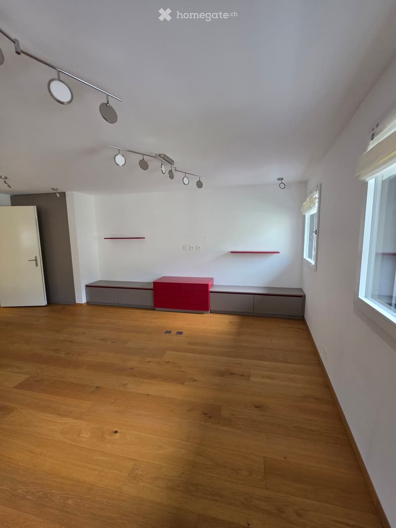 Empty room with wooden flooring, white walls, and modern lighting fixtures. Features a built-in cabinet and a small red shelf.