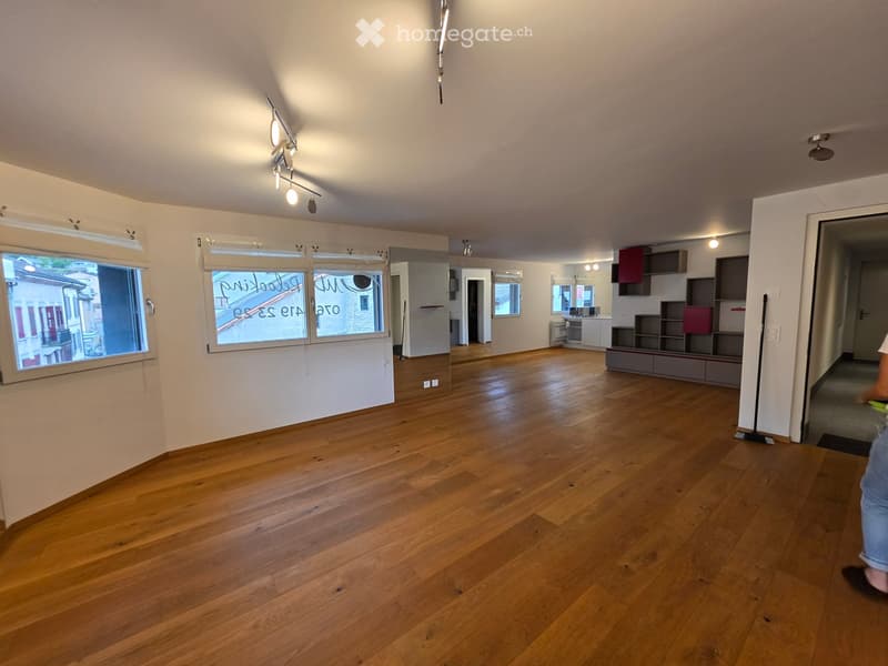 Empty room with wooden flooring, white walls, large windows, and track lighting. No furniture or equipment present.