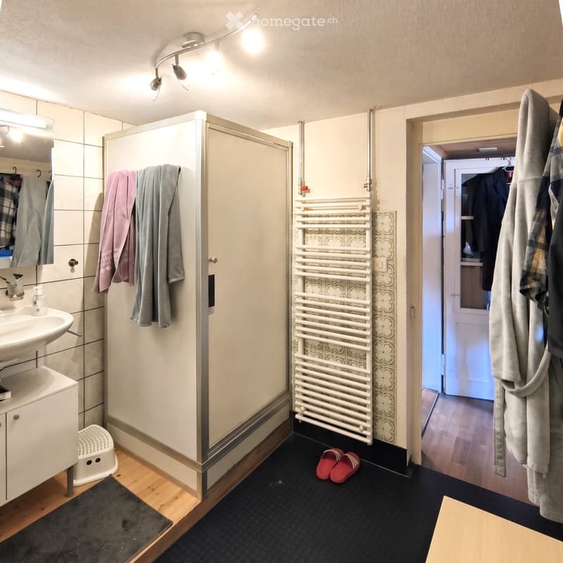 Modern bathroom with a sink, mirror, radiator, towel rack, bathrobe, and bathroom slippers.