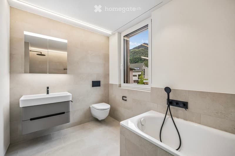 Modern bathroom with a large window offering a scenic view, featuring a sink, toilet, bathtub, and a large mirror.