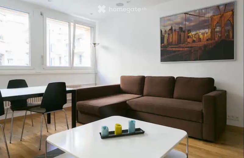 Spacious living room with large windows, brown sofa, white coffee table, and a framed cityscape artwork on the wall