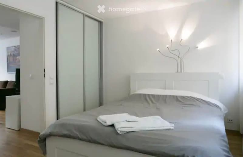 Spacious bedroom with sliding glass doors, white walls, gray bedding, and a modern decor with a vase on the dresser