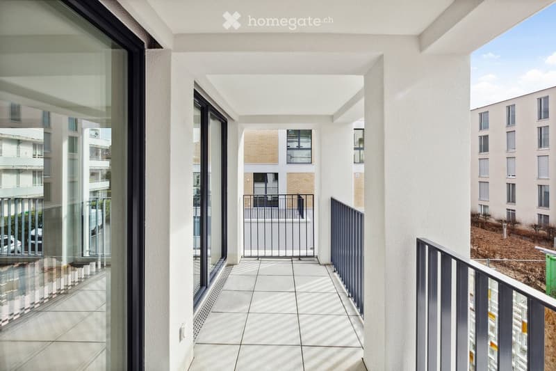 Modern balcony with white tiled flooring, glass railings, and views of surrounding buildings and greenery.