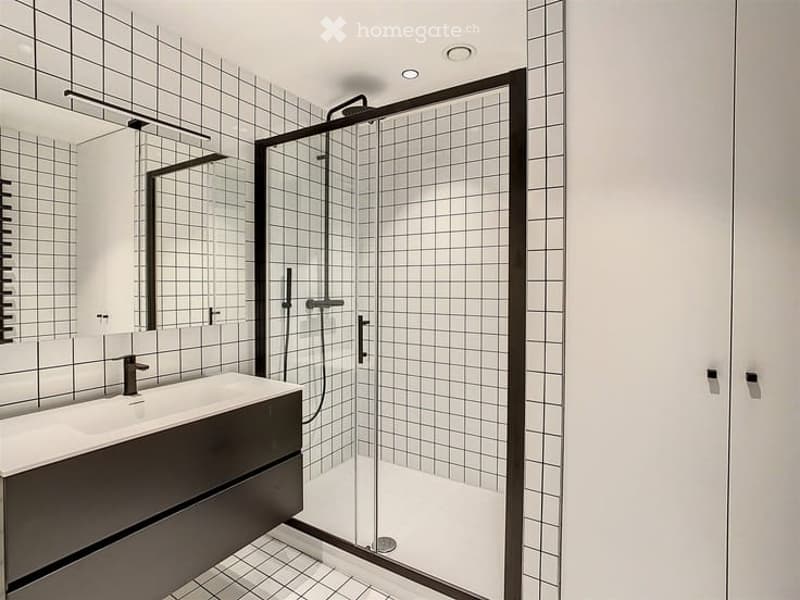Modern bathroom with white tiled walls, a dark wooden vanity with a sink, a large mirror, and a glass-enclosed shower stall.