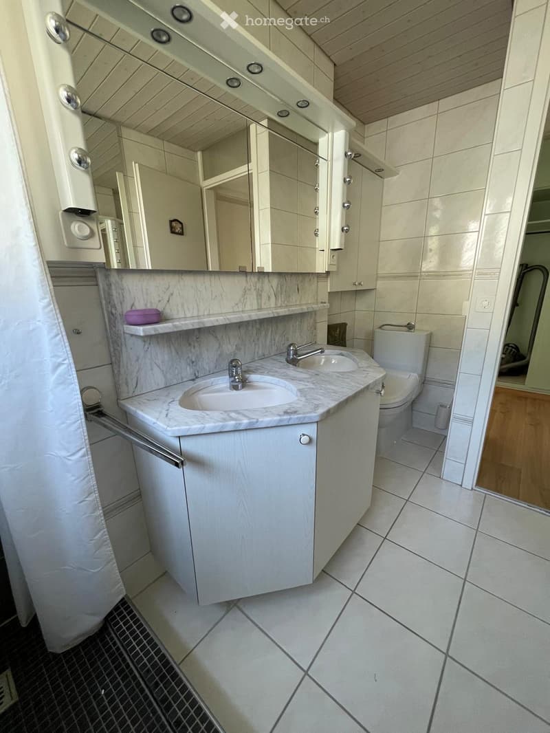 Modern bathroom with white tiled walls and floor, marble countertop, double sink, mirror, and toilet.