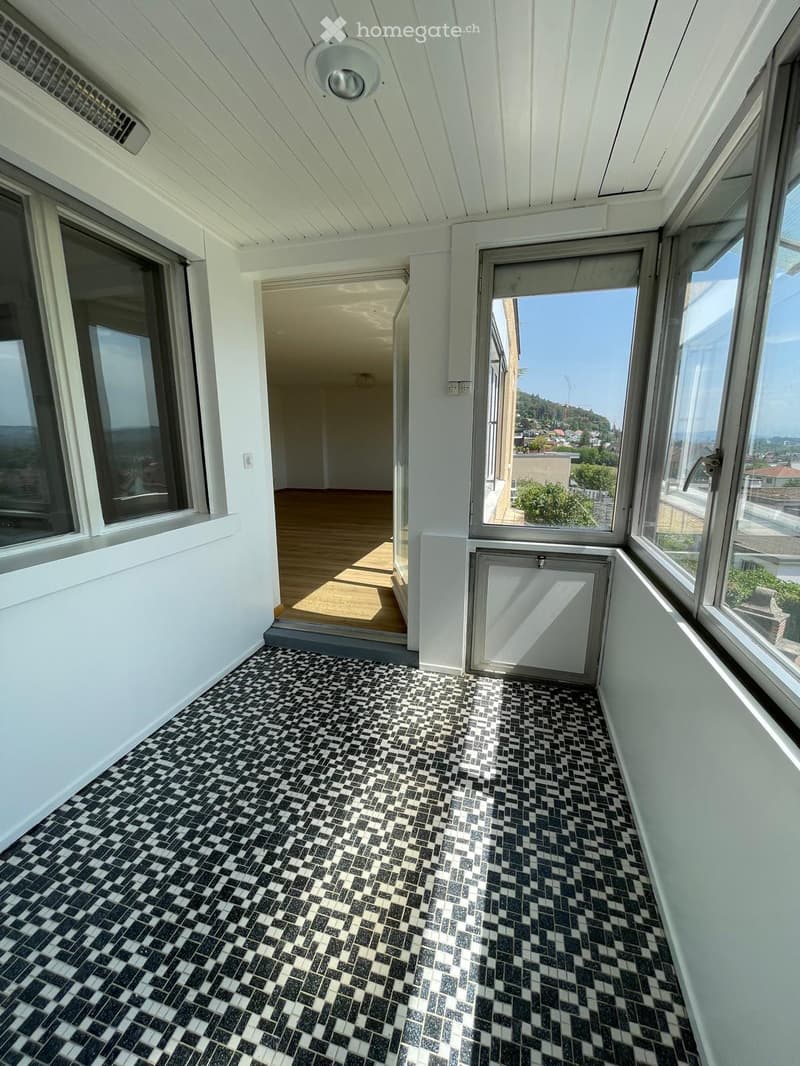 Balcony with black and white checkered tiles, large windows, and a view of the city and hills.