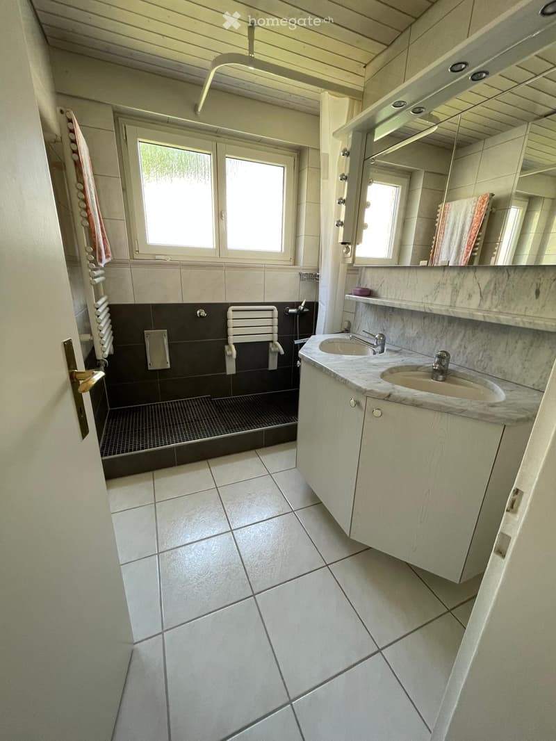 Bathroom with a double sink, marble countertop, large mirror, radiator, and tiled floor.