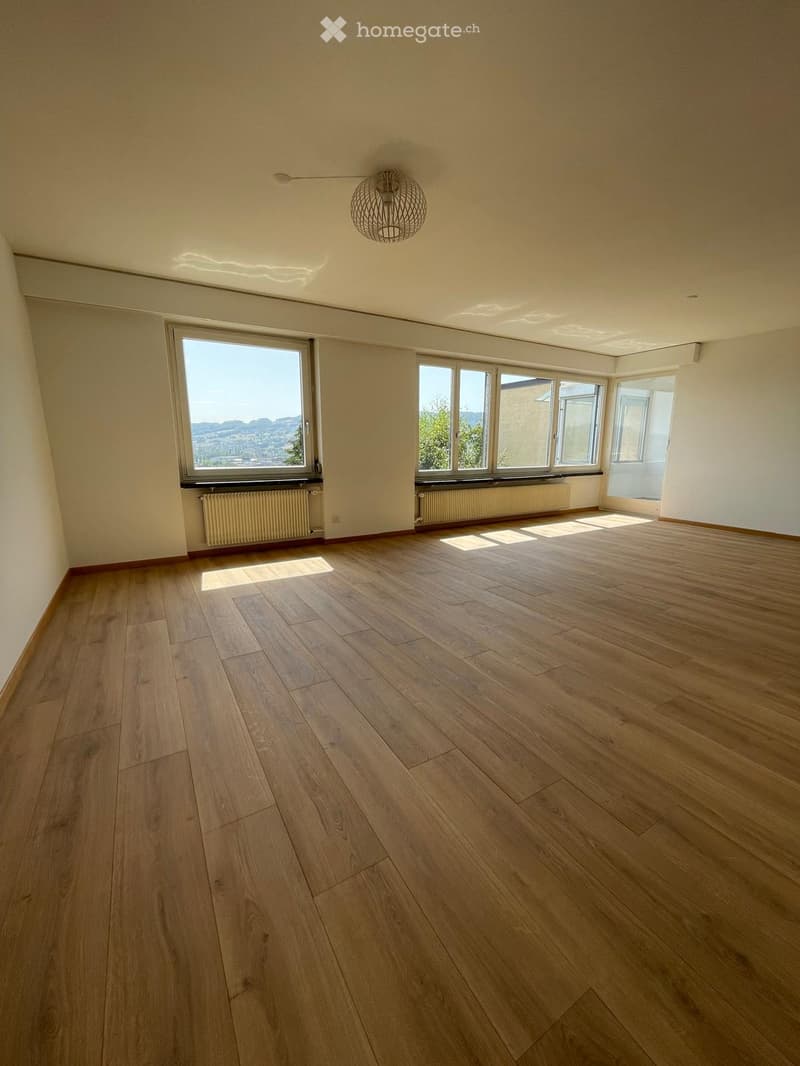 Empty room with wooden flooring, large windows, and a modern pendant light fixture.