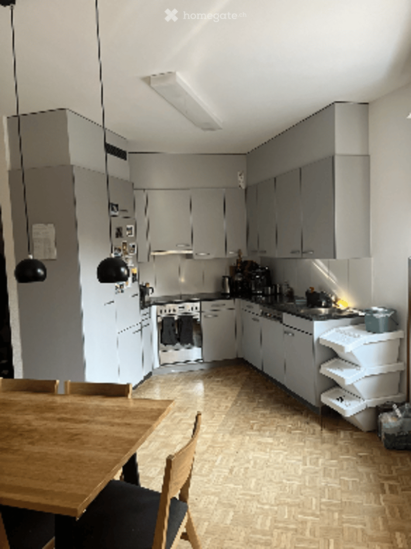 Modern kitchen with grey cabinets, white appliances, and a wooden dining table with chairs.