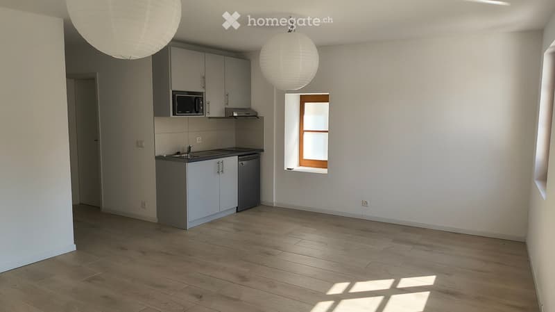 Modern kitchen with light grey cabinets, a microwave, a sink, and a dishwasher. The space features wooden flooring and large windows allowing natural light to fill the room.