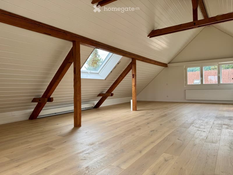 Empty attic space with wooden beams, skylight, and wooden flooring.