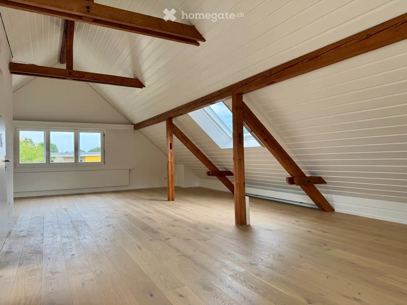 Empty attic space with wooden beams, skylight, and wooden flooring.