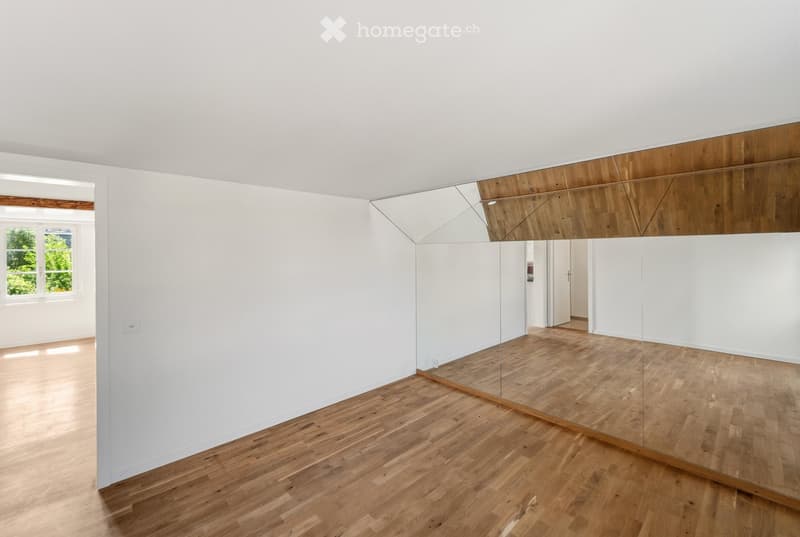 Completely empty room with white walls, wooden floor, and large mirror on one wall. No furniture or equipment.