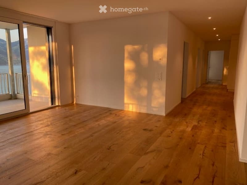Empty room with wooden flooring, large sliding glass door leading to a balcony with a scenic view, and bright natural light.