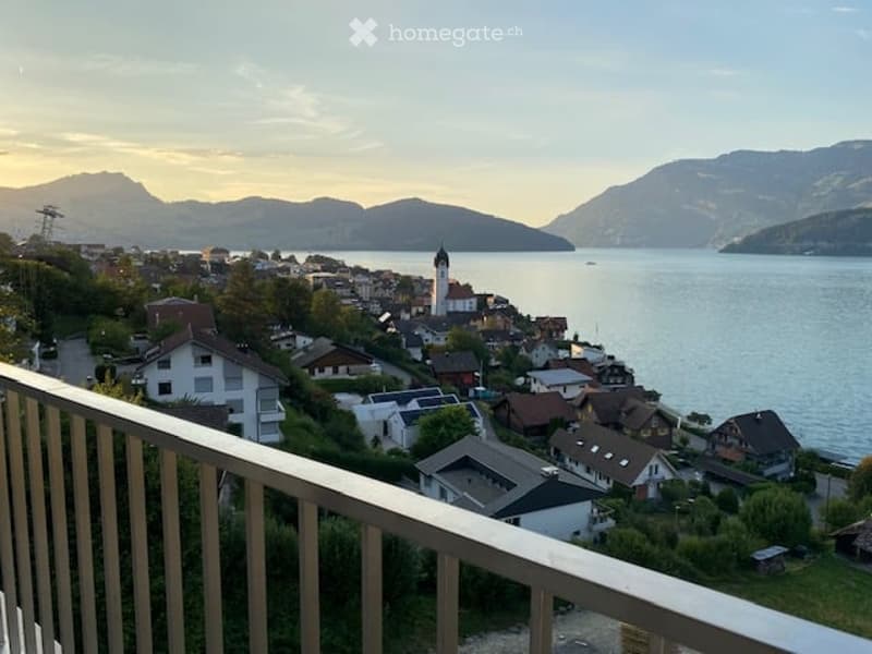 Balcony overlooking a picturesque lakeside town with houses, a church, and mountains in the background.