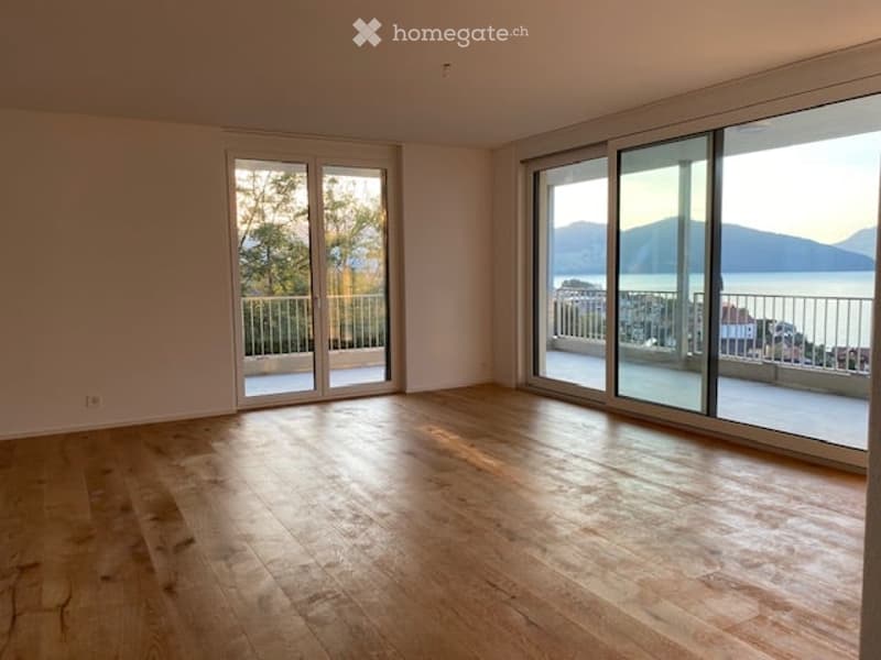 Bright, unfurnished room with large sliding glass doors leading to a balcony, wooden flooring, and scenic mountain and sea views.