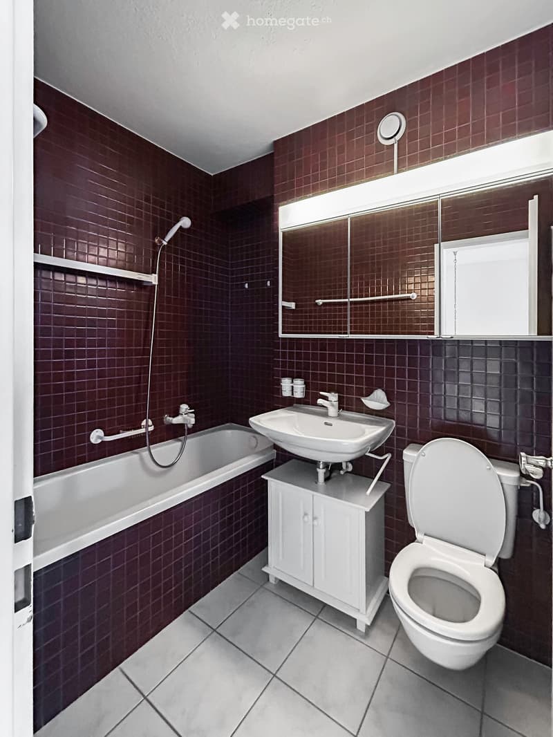 Bathroom with dark red tiled walls, white bathtub, sink, toilet, and a mirrored cabinet above the sink.