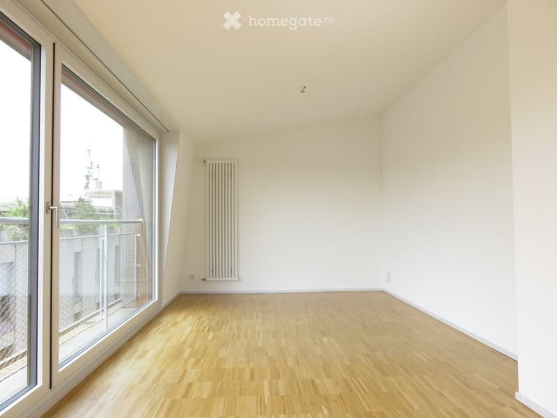 Empty room with wooden flooring, white walls, large window with a view, and a radiator on the wall.