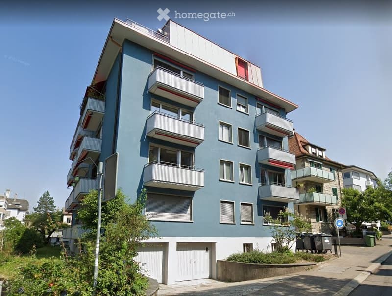 Modern multi-story apartment building with blue facade, white balconies, and garage entrances.